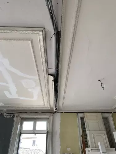 Cette image représente un chantier en cours de réalisation pour la réfection d'un plafond traditionnel en lattis plâtre avec des corniches et moulures staff